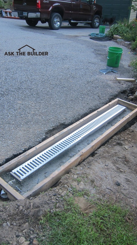 This trench drain will collect water that’s rushing off the driveway. More concrete needs to be added between the drain body and the wood form. Photo Credit: Tim Carter